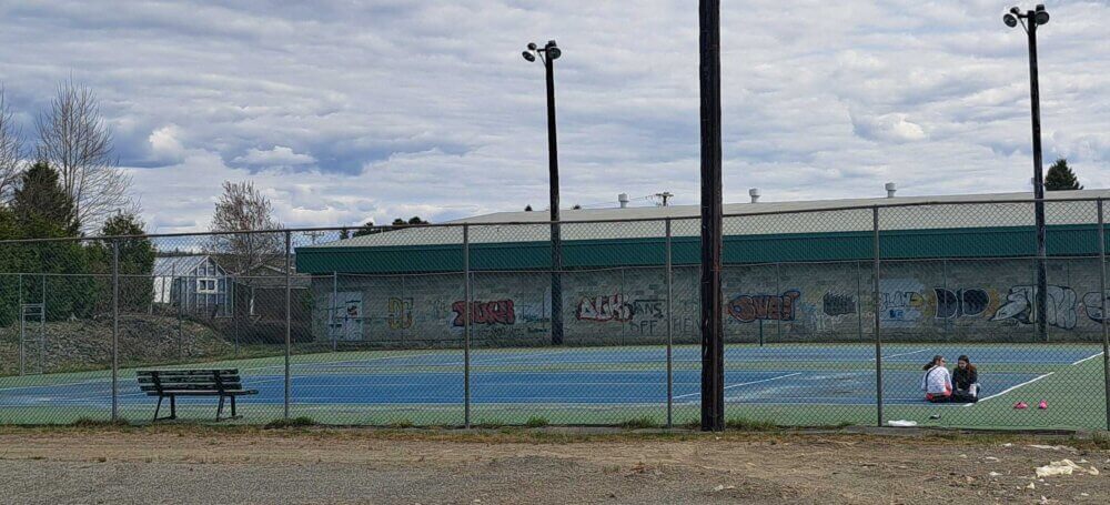 Terrain de tennis clôturé lors d'une journée de printemps nuageuse.